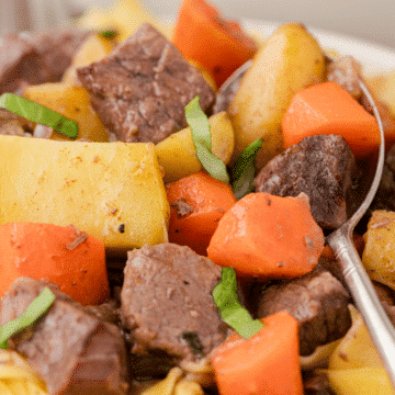 a close up of crock pot beef stew with gravy including beef, carrots, and potatoes