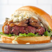 a close up of a homemade black and blue burger with sauteed onions and mushrooms, blue cheese, and arugula