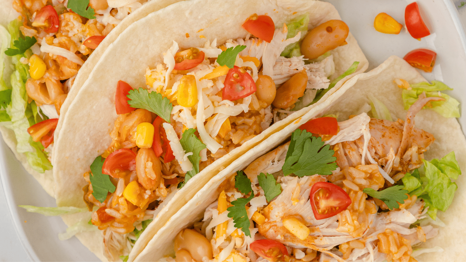 a close up of Instant Pot chicken tacos with beans, rice, tomatoes, corn, cheese, and cilantro