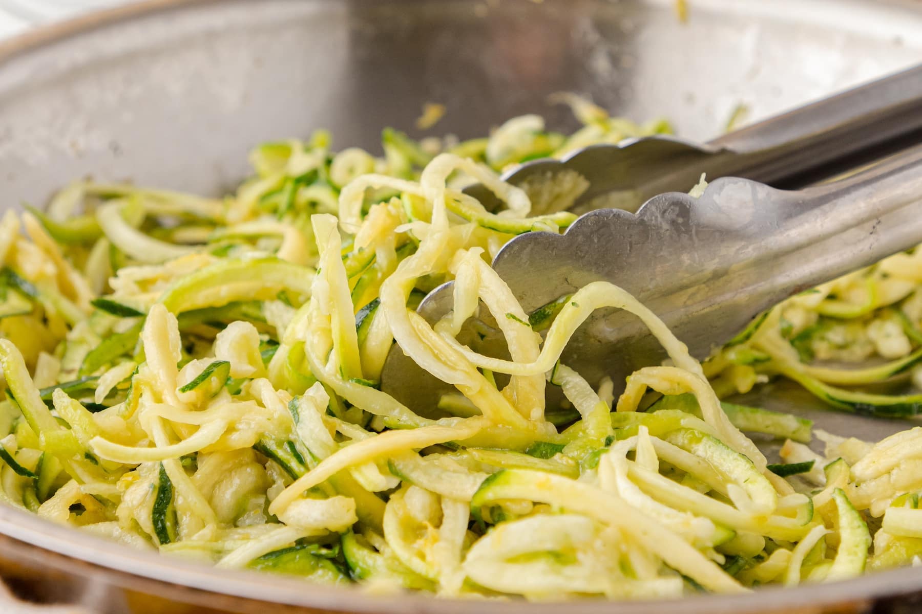 lemon zucchini noodles in a skillet with silver tongs