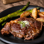 air fryer ribeye steak on a black plate with roast potatoes and asparagus