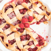 homemade raspberry pie topped with fresh raspberries with one slice missing in a white pie plate