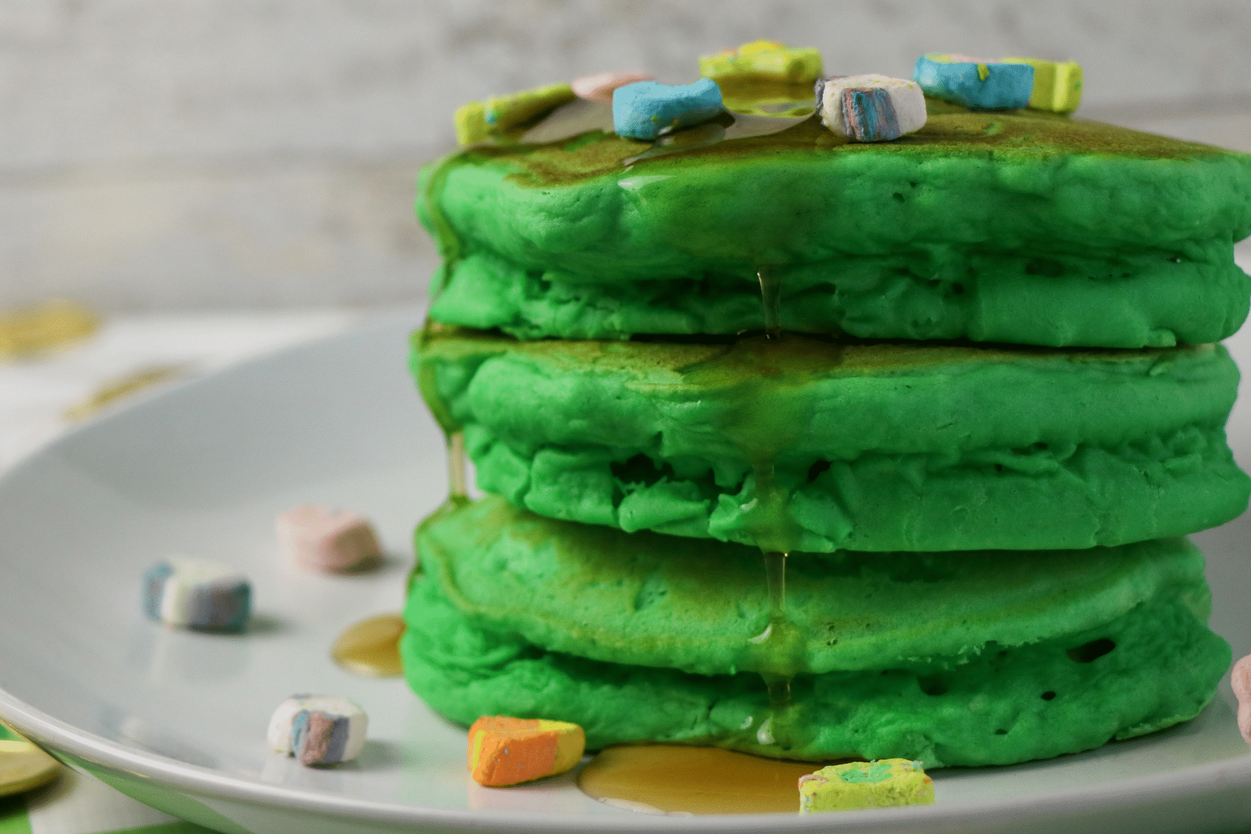 a stack of green Lucky Charms pancakes topped with maple syrup and Lucky Charms marshmallows