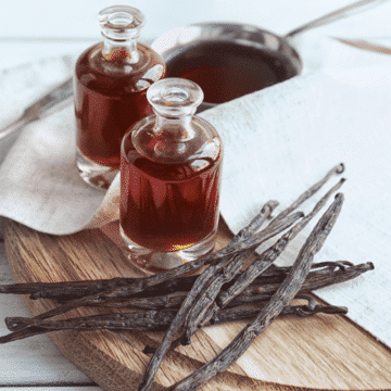 two bottles of vanilla extract with a bunch of vanilla beans on a wooden cutting board