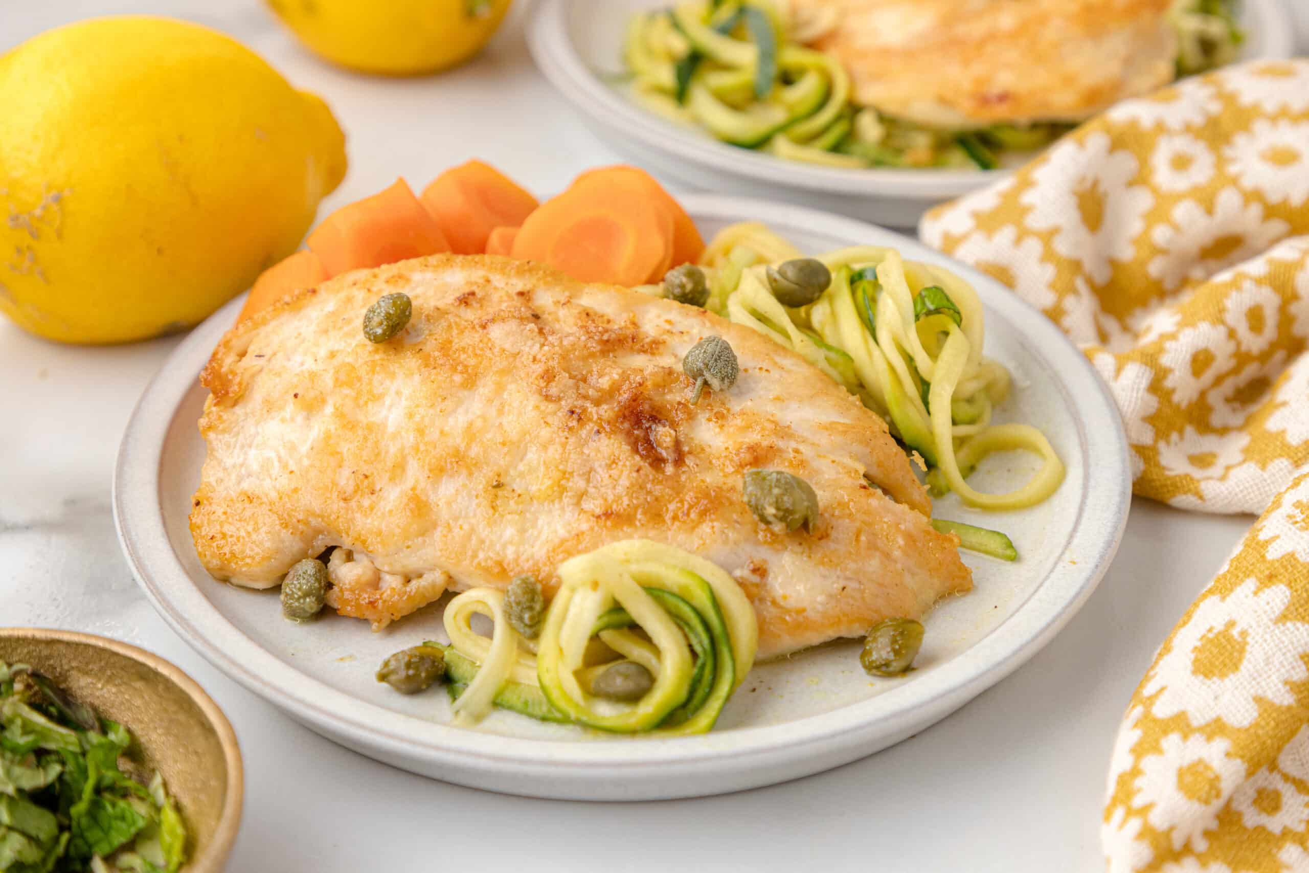 healthy chicken piccata with zucchini noodles on a white plate with carrots