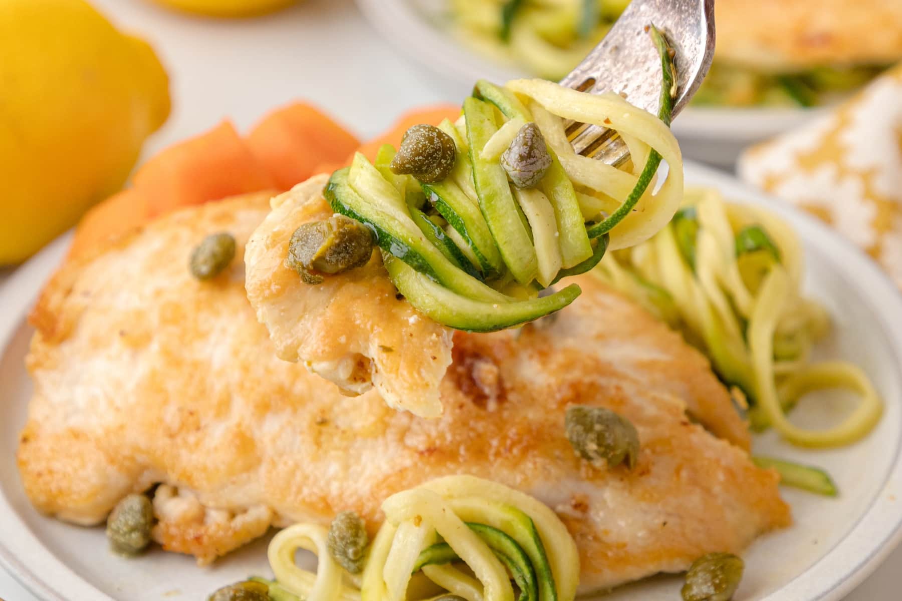 healthy chicken piccata with capers and zucchini noodles on a fork in front of a plate of the same
