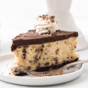 one slice of chocolate peppermint cheesecake with an oreo crust topped with whipped cream and chopped chocolates on a white plate with a fork