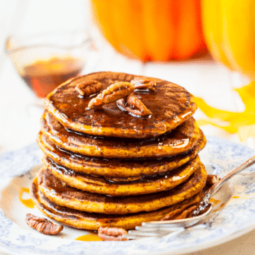 pumpkin pie pancakes topped with syrup and pecans on a blue and white plate with a fork