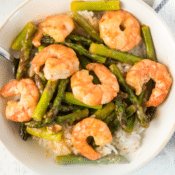 shrimp and asparagus stir fry over rice in a white bowl