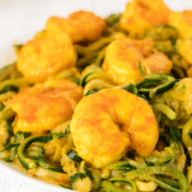 a close up of spicy sriracha shrimp with peanut zucchini noodles on a white plate