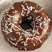 a close up of one baked vegan chocolate donut with chocolate frosting and white sprinkles