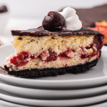 a close up of a slice of chocolate cherry cheesecake with oreo crust on a stack of white plates