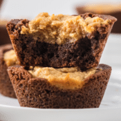 two peanut butter cheesecake brownies in a stack on a white plate, the top one is bitten in half