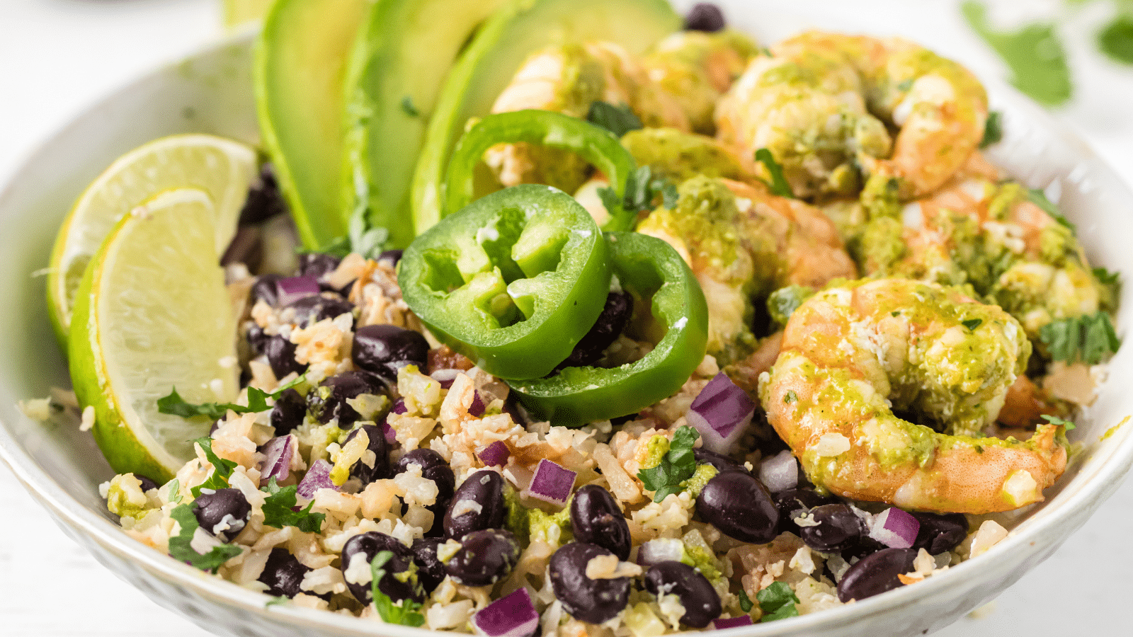 a side view of cilantro lime shrimp burrito bowl with rice and beans in a white bowl