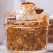 pumpkin pie overnight oats in a small mason jar topped with whipped cream and pecans
