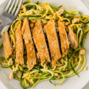 a close up of peanut sesame chicken over zucchini noodles on a white plate with a fork