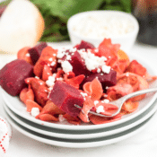 roasted chicken with red beets and noodles topped with feta cheese on a stack of white plates with a fork