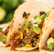 a close up of Instant Pot shredded beef tacos with chopped avocado and fresh cilantro