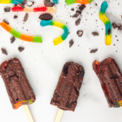 three of the best dirt pudding popsicles with gummy worms and Oreo crumbs on a white background