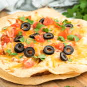 a close up of one Mexican pizza topped with cheese, black olives, and tomatoes on a cutting board