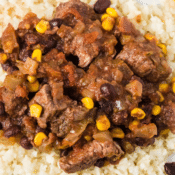 a close up of Crockpot Mexican steak and beans with corn and onions on a bed of rice