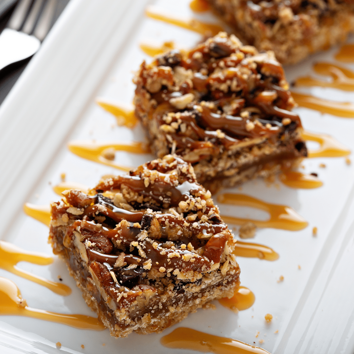 three pecan pie bars on a plate with caramel sauce