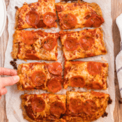 a hand picking up one slice of chicken crust pizza on parchment paper