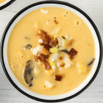 creamy cheesy vegetable soup topped with bacon in a white bowl with a black rim