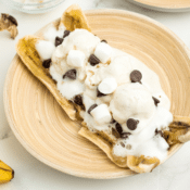 one microwave banana boat sundae with chocolate chips and marshmallows on a tan colored plate