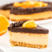 one slice of chocolate orange cheesecake on a white plate with the rest of the cheesecake in the background