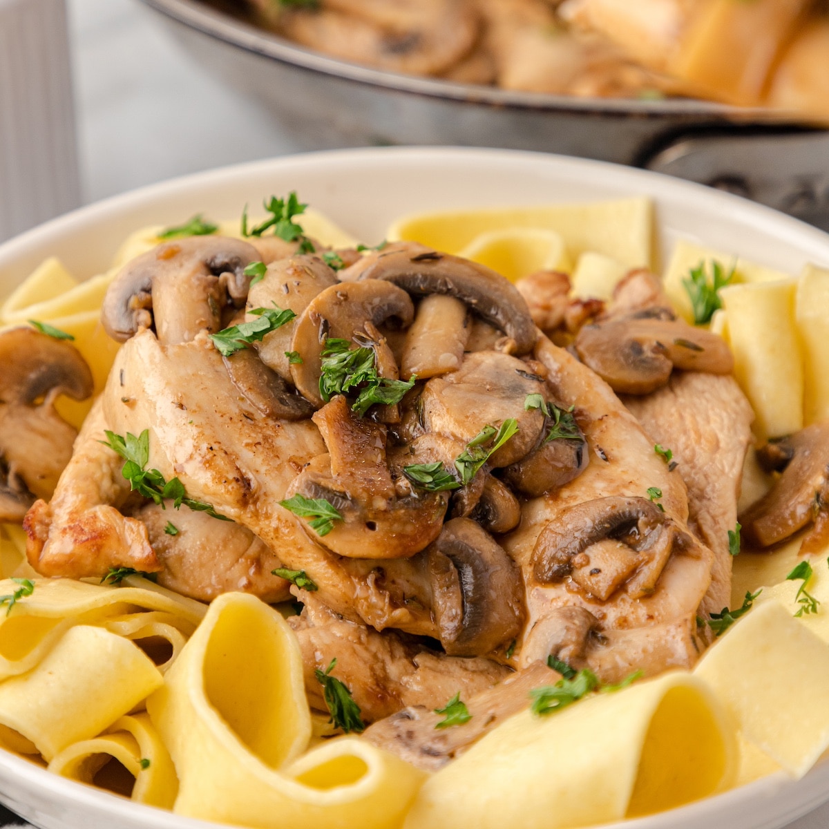 balsamic chicken and mushrooms over noodles on a white plate