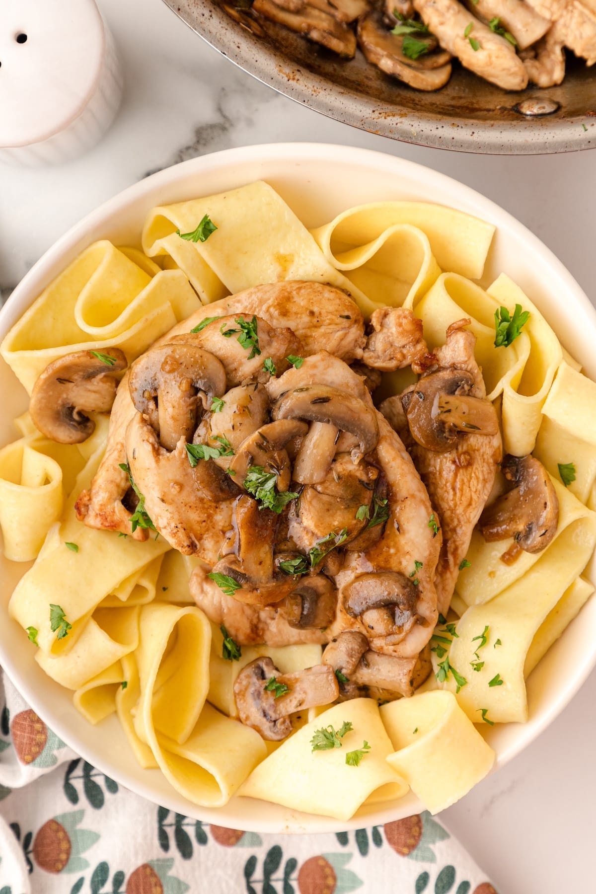 balsamic chicken and mushrooms over noodles on a white plate with chopped parsley