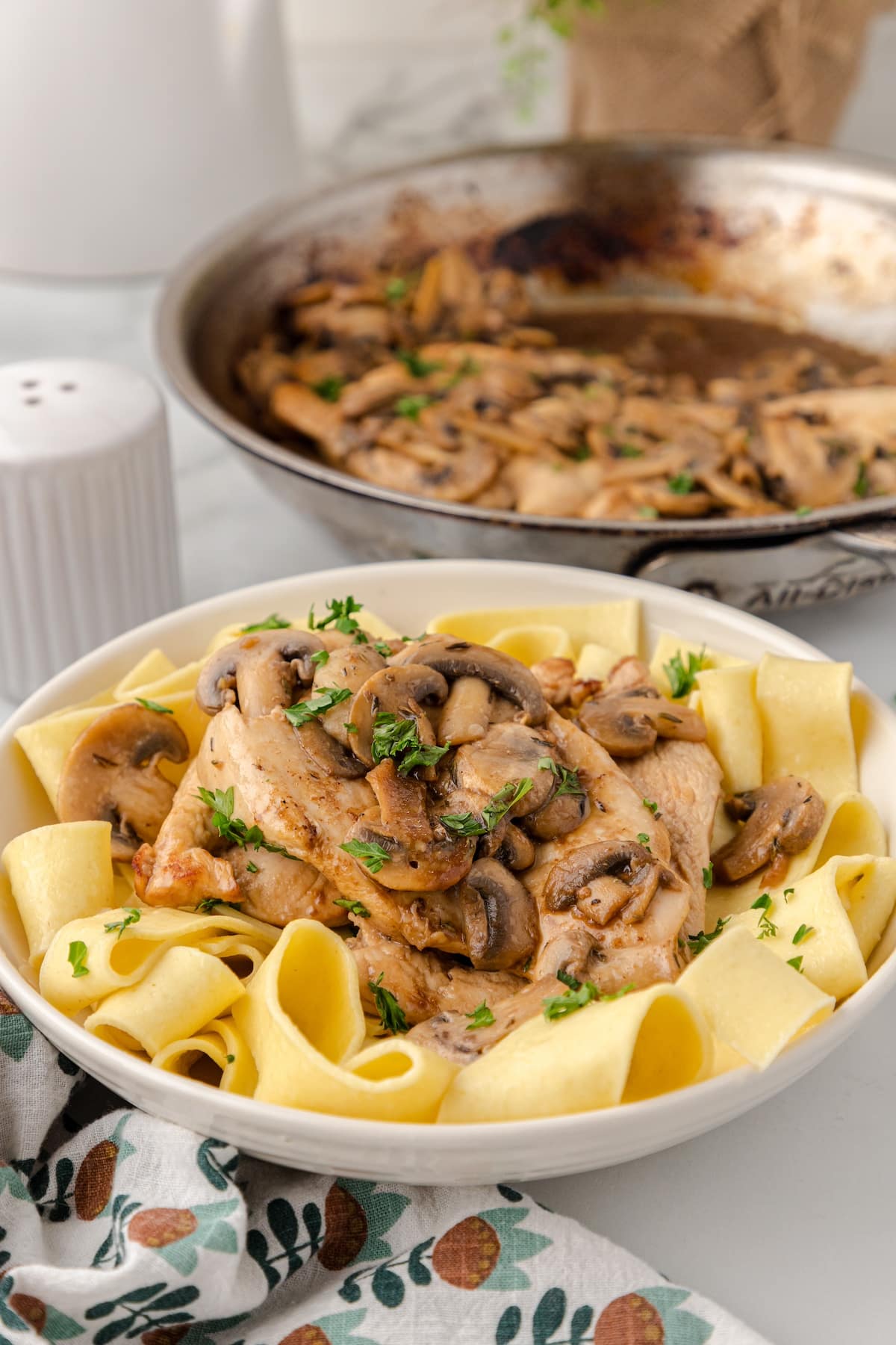 balsamic chicken and mushrooms over noodles on a white plate with a full skillet in the background