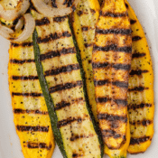 a close up of grilled zucchini and yellow squash planks, and onions on a white platter