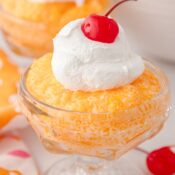 orange fluff salad in a glass dish topped with whipped cream and a maraschino cherry