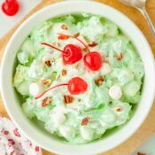 pistachio fruit salad in a white bowl topped with three maraschino cherries
