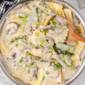 a big skillet full of ravioli alfredo with mushrooms and asparagus