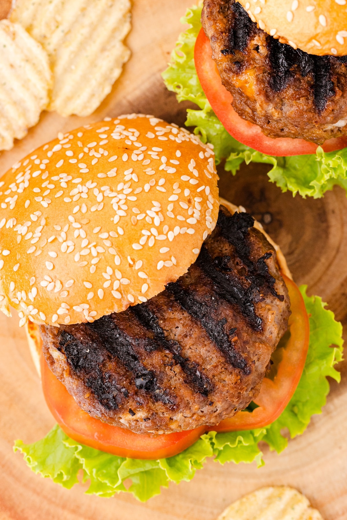 BBQ hamburgers on sesame seed buns with lettuce and tomatoes and potato chips