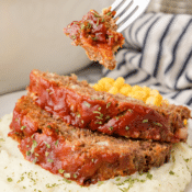a forkful of crockpot meatloaf with a plate of mashed potatoes and meatloaf in the background