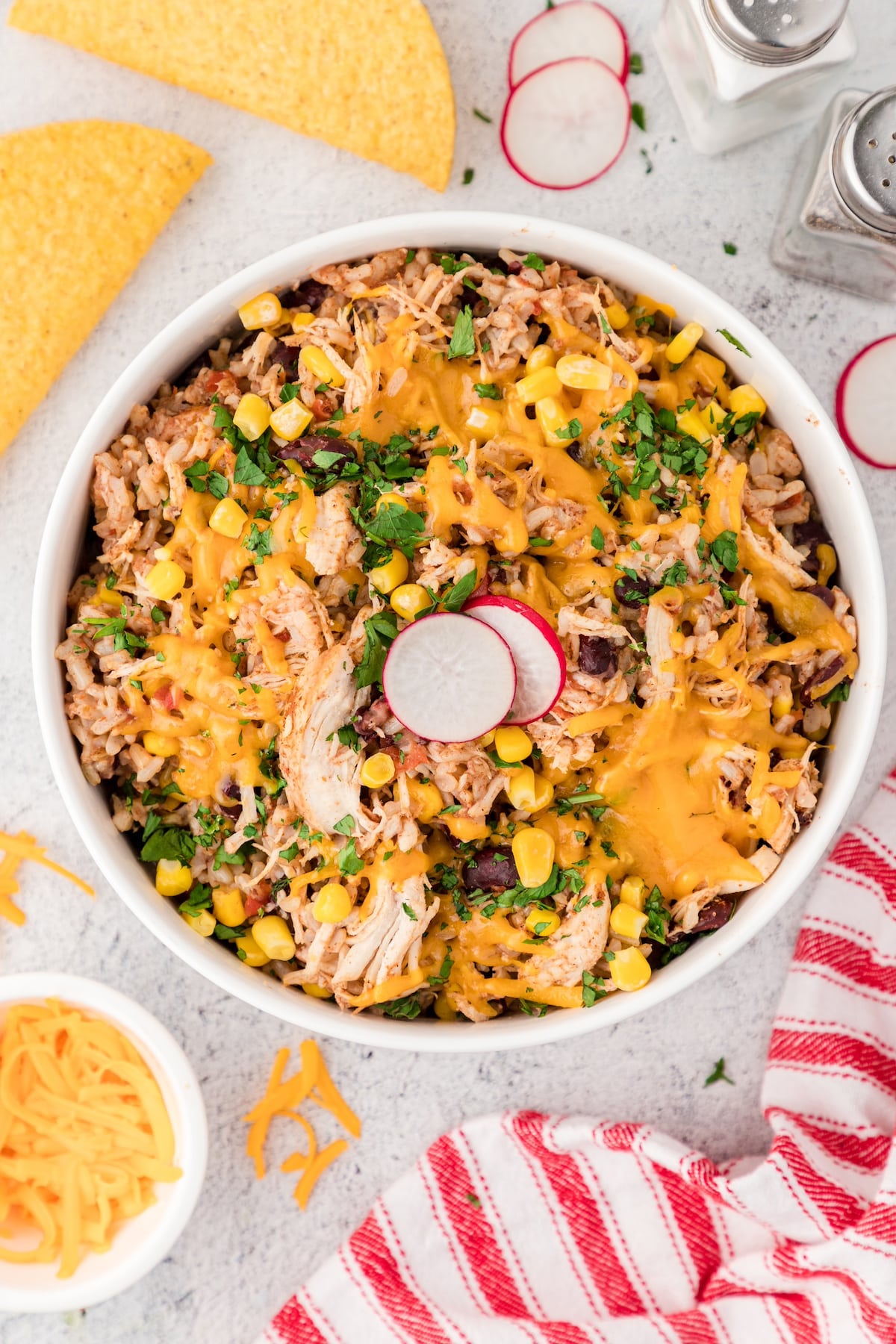 Instant Pot cheesy chicken and rice topped with shredded cheddar cheese and fresh cilantro and two slices of radish in a large white serving bowl