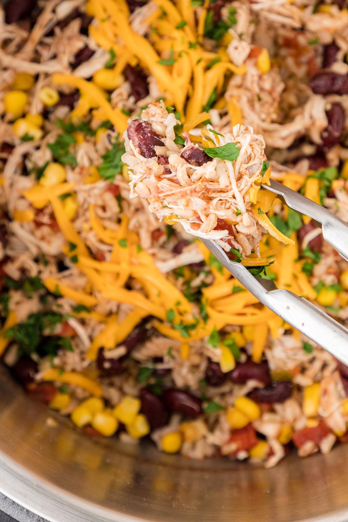 tongs holding a bite of cheesy chicken and rice with beans and corn over the Instant Pot