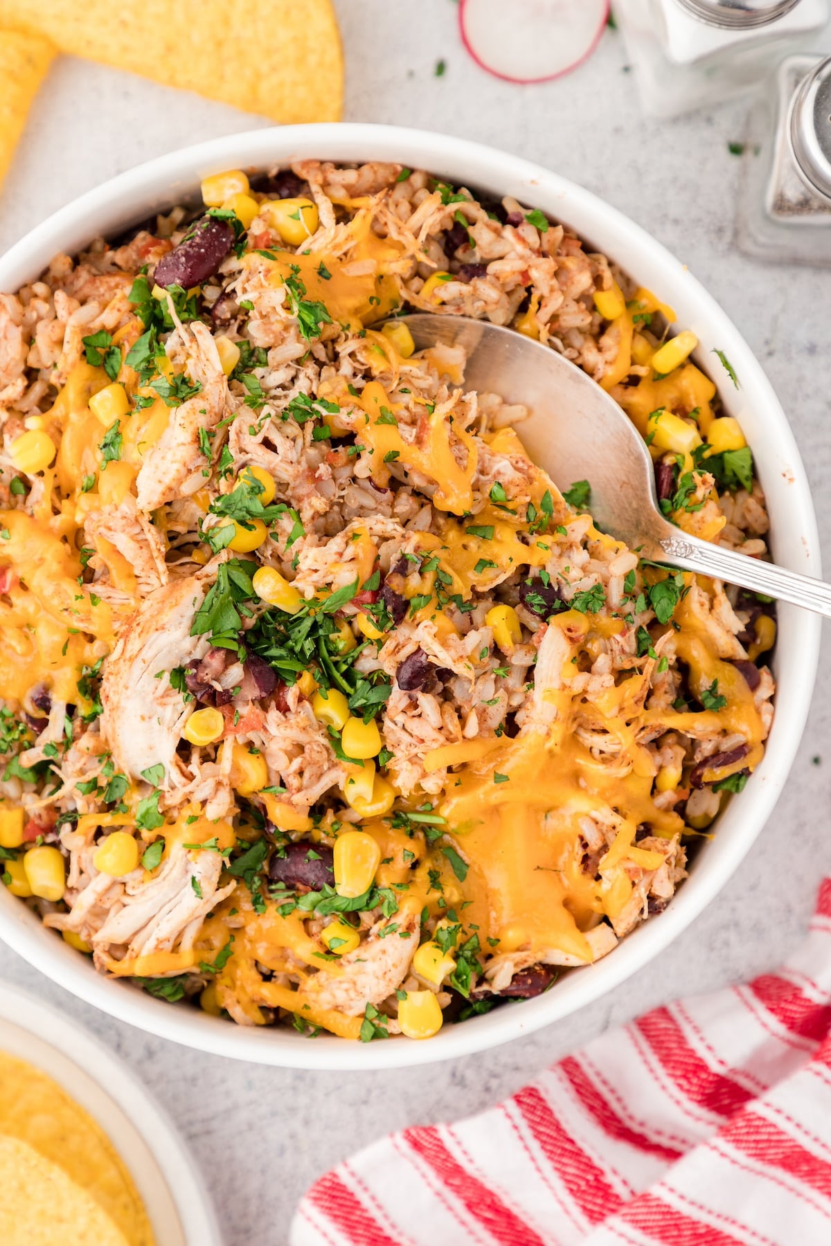 Instant Pot cheesy chicken and rice with beans and corn in a white serving bowl with a big silver serving spoon