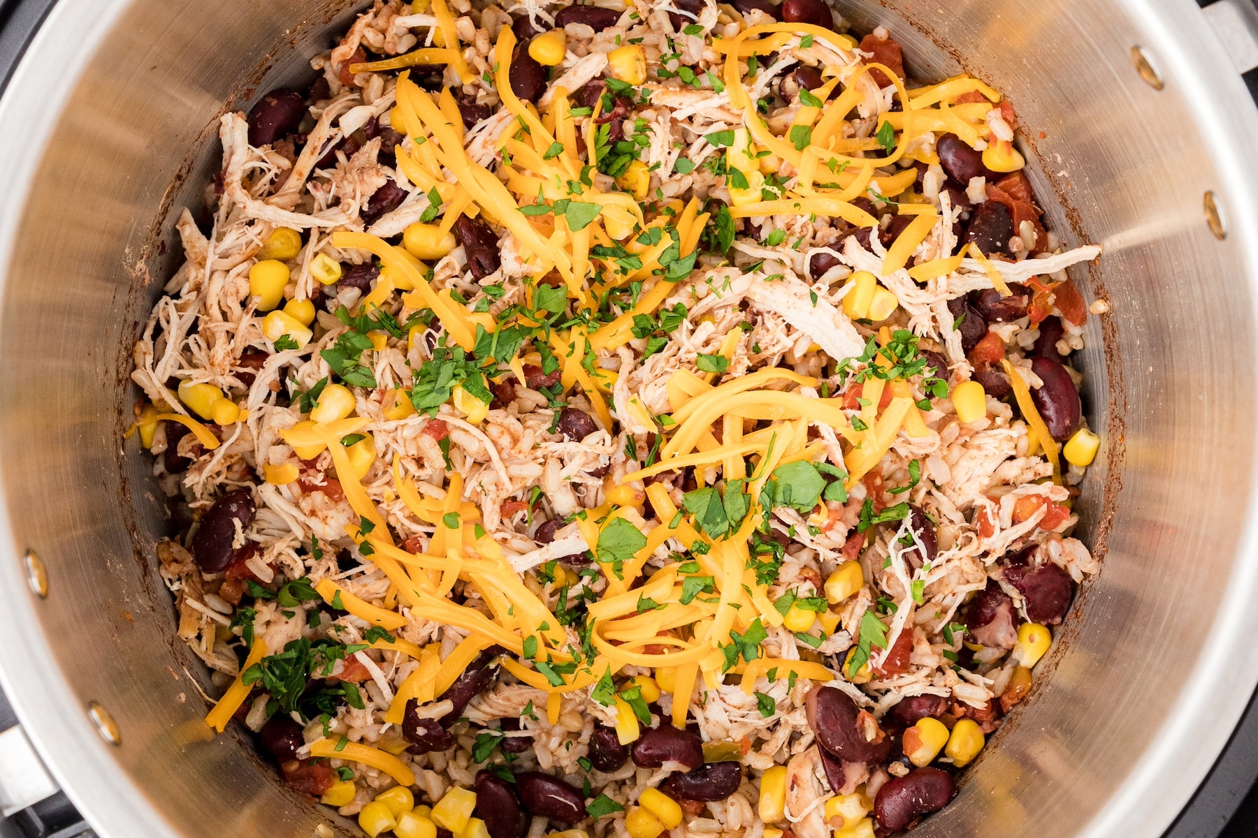 a close up of cheesy chicken and rice with beans and corn topped with shredded cheddar cheese and fresh cilantro in the Instant Pot