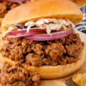 a close up of one Instant Pot sloppy joe sandwich with slices of red onion and coleslaw on top and BBQ meat spilling out