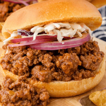 a close up of one Instant Pot sloppy joe sandwich with slices of red onion and coleslaw on top and BBQ meat spilling out