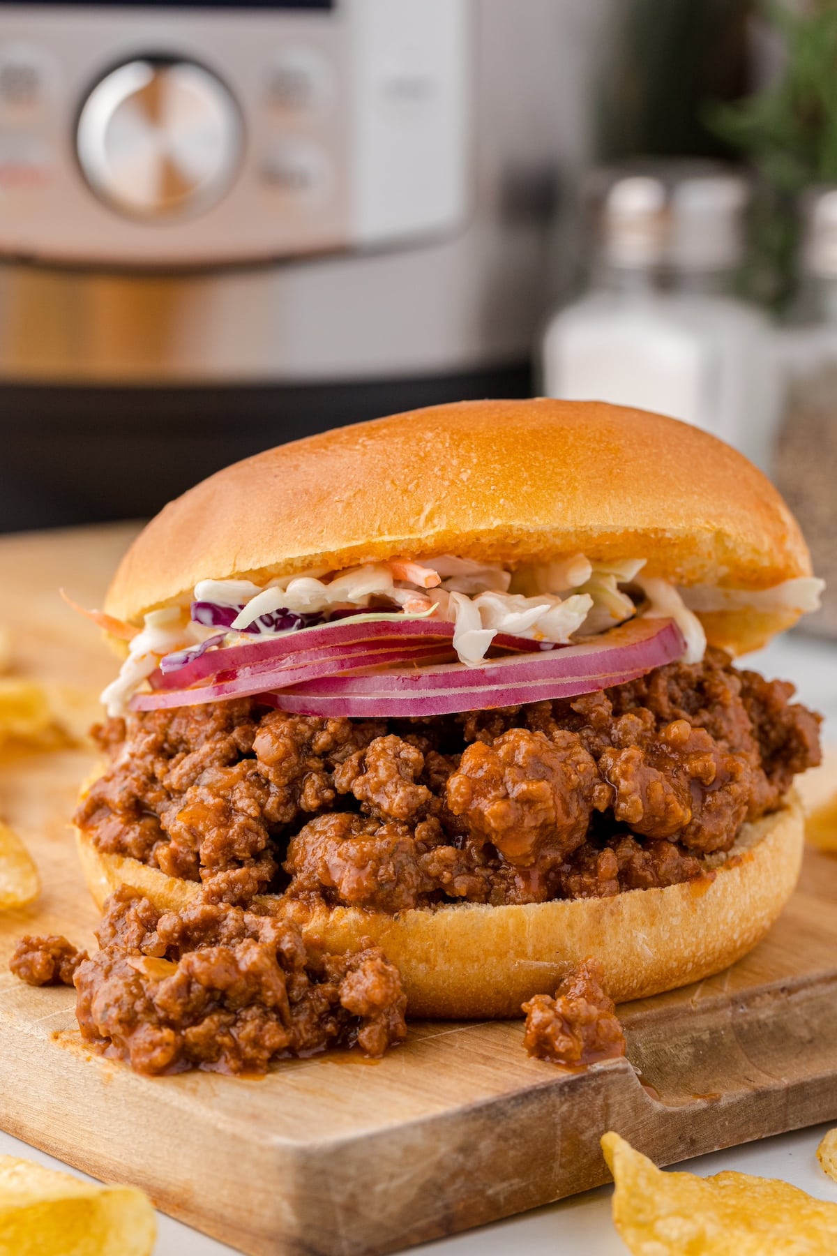 one Instant Pot sloppy joe sandwich with slices of red onion and coleslaw on top with an Instant Pot in the background