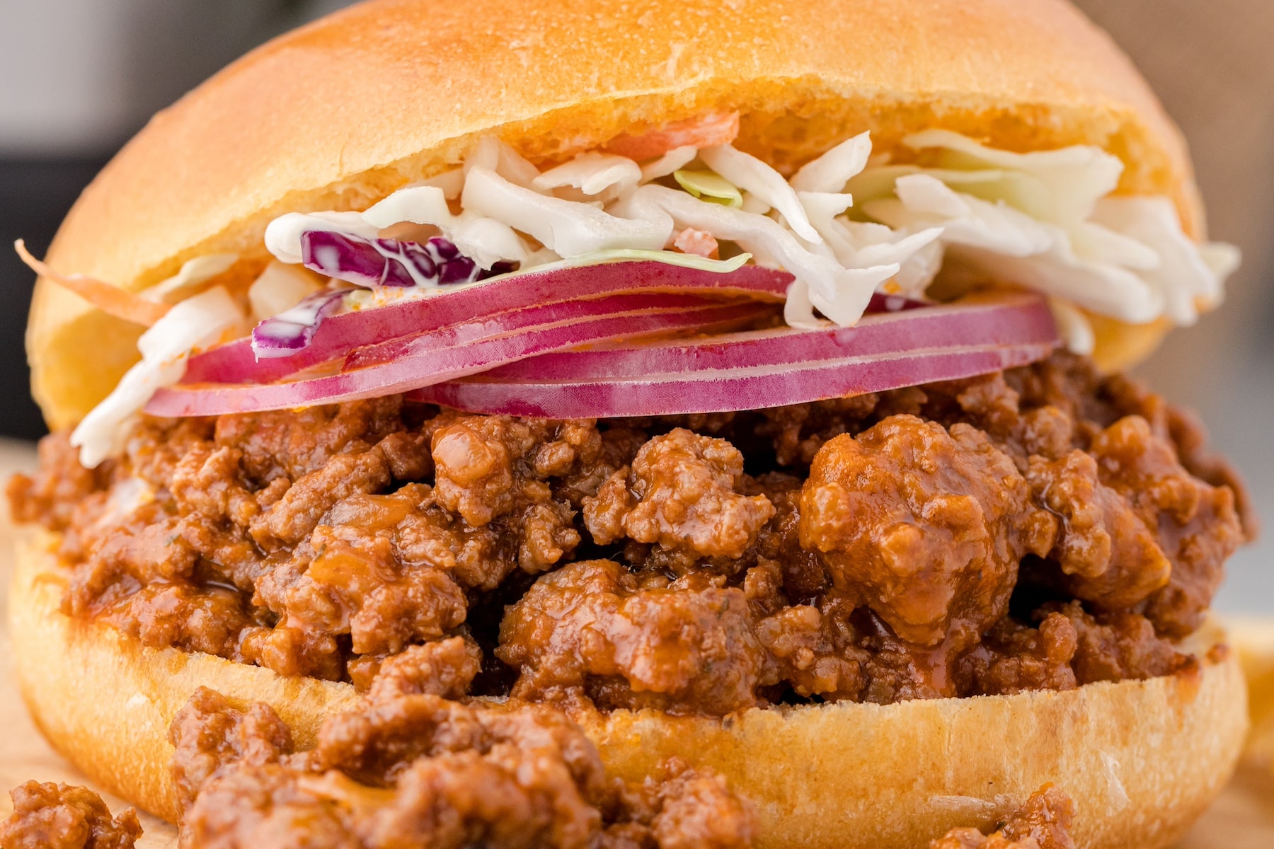 a close-up of one Instant Pot sloppy joe sandwich with slices of red onion and coleslaw on top