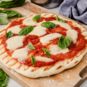 the best grilled pizza dough topped with tomato sauce, mozzarella cheese, and fresh basil on a cutting board