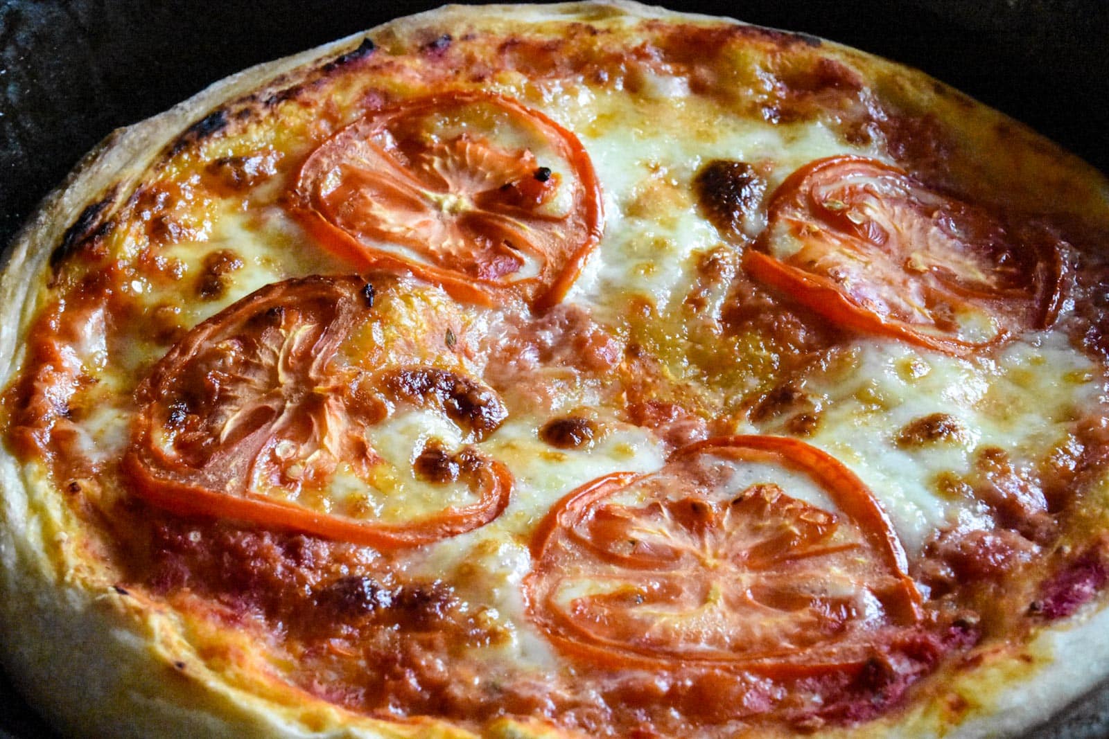 a close up of sourdough pizza crust topped with cheese and sliced tomatoes