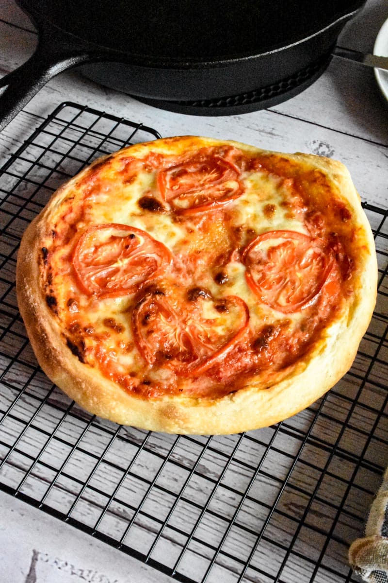 sourdough pizza with cheese and sliced tomatoes on a wire rack
